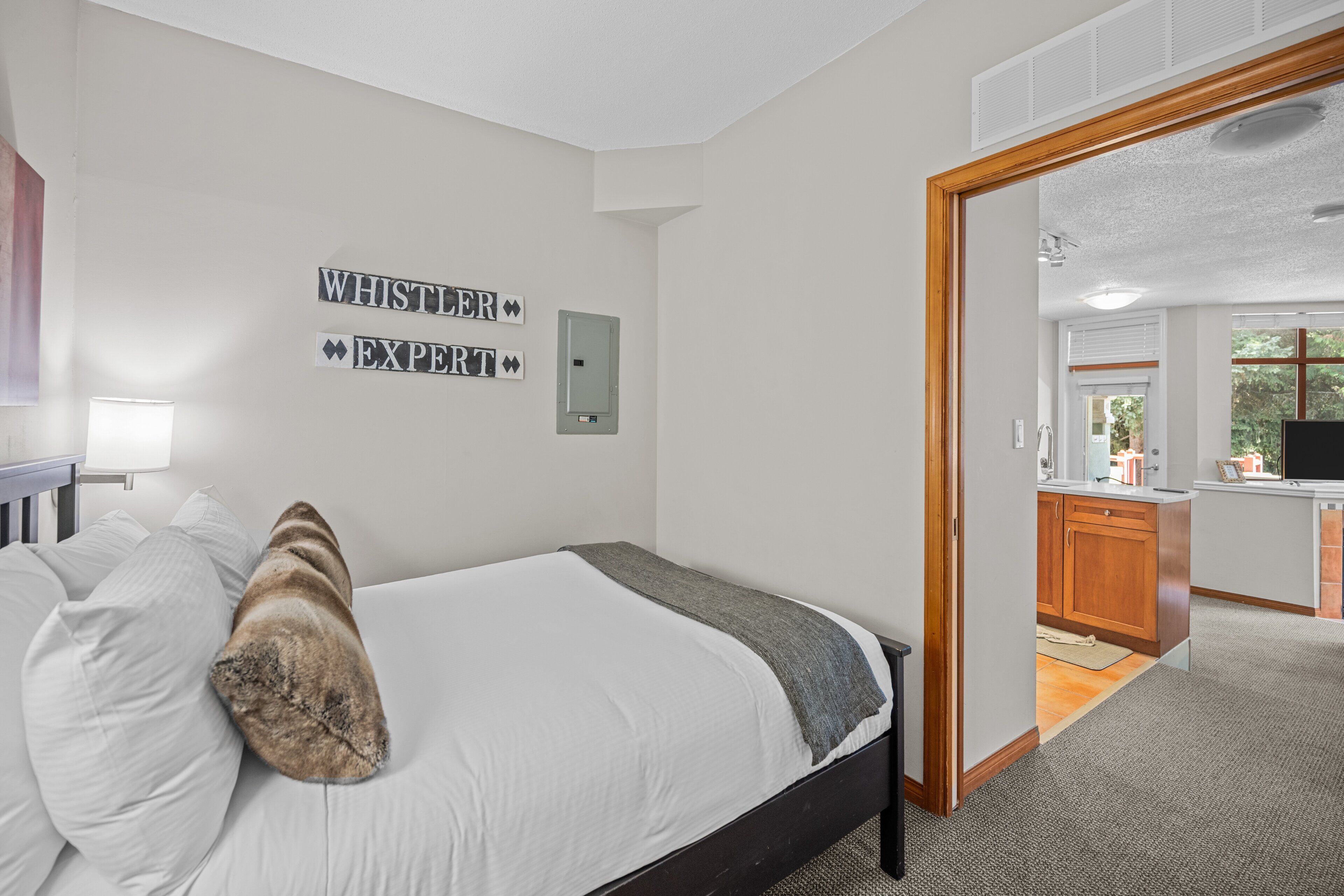 A bedroom with a bed, a bedside table, a lamp, and a wall-mounted sign.