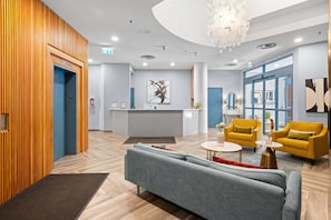 A modern lobby with a reception desk, a grey sofa, yellow armchairs, and a wooden wall.