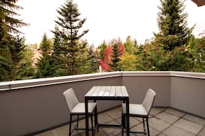 A balcony with a table and chairs, surrounded by trees and a view of buildings. - Alpenglow Lodge Legacy Studio by MVA (Whistler)
