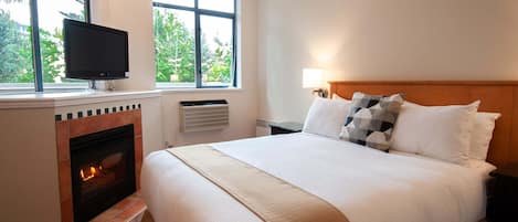 Quarto de hotel com cama, televisão, lareira e janela com vista para árvores.