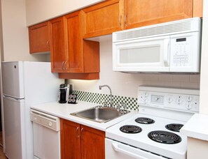 A kitchen with wooden cabinets, a white refrigerator, a microwave, a coffee maker, a sink, and a stove. - Alpenglow Lodge Legacy Studio by MVA (Whistler)