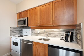 A modern kitchen with wooden cabinets, stainless steel appliances, a tiled backsplash, and a coffee maker. - Alpenglow Lodge Junior Penthouse by MVA (Whistler)
