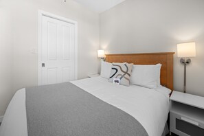 Una habitación de hotel con cama, mesita de noche, lámpara y puerta.