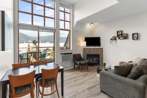 A modern living room with a fireplace, a TV, and a dining area with chairs and a table. - Alpenglow Lodge Junior Penthouse by MVA (Whistler)