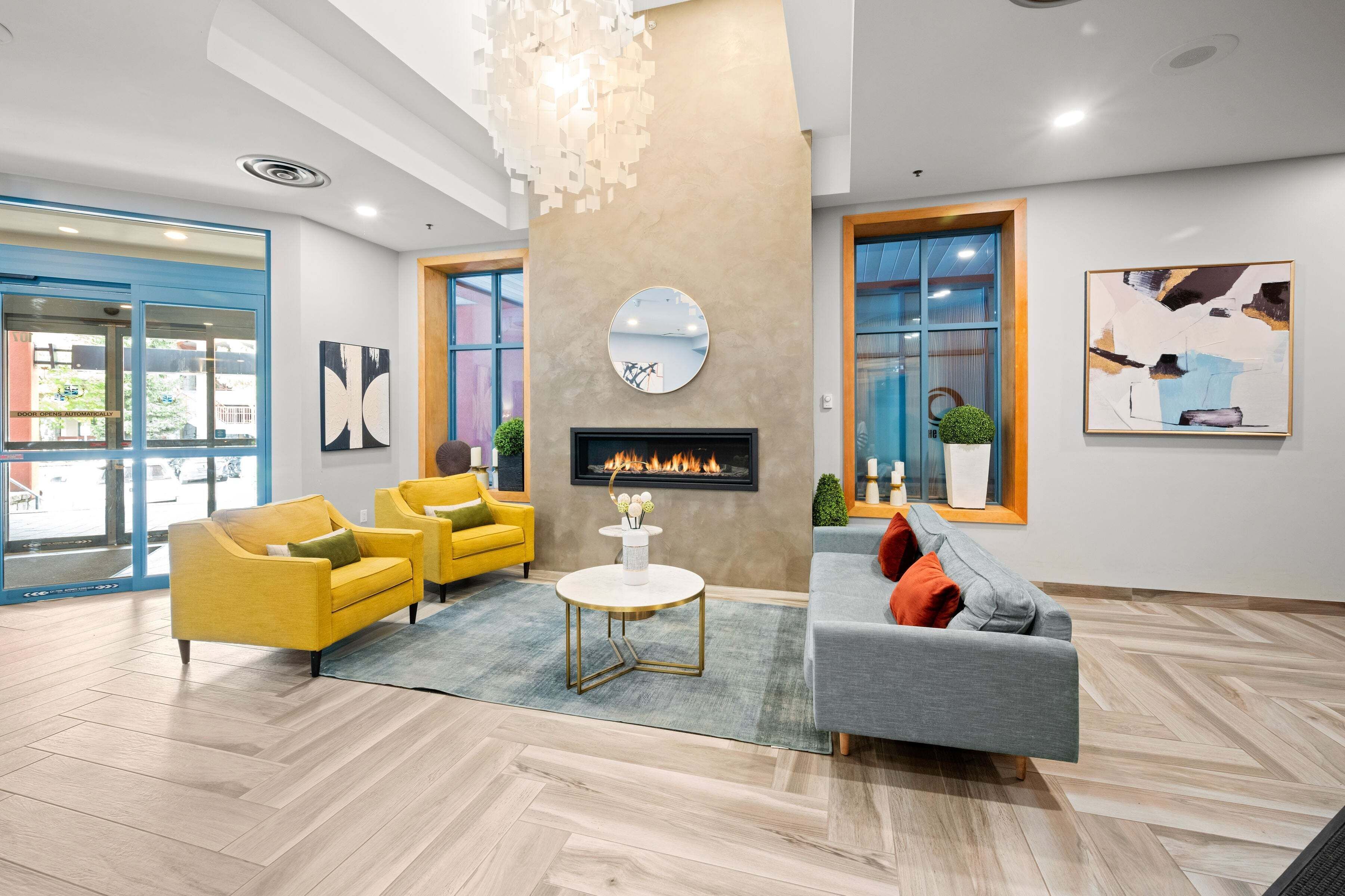 A modern lobby with a fireplace, yellow and grey sofas, and a large mirror on the wall.