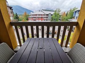 A balcony with a view of a town square, buildings, and mountains. - Bear Lodge One Bedroom by MVA (Whistler)