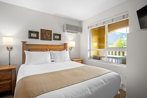 A bedroom with a large bed, bedside lamps, a window with a view, and wall-mounted artwork.