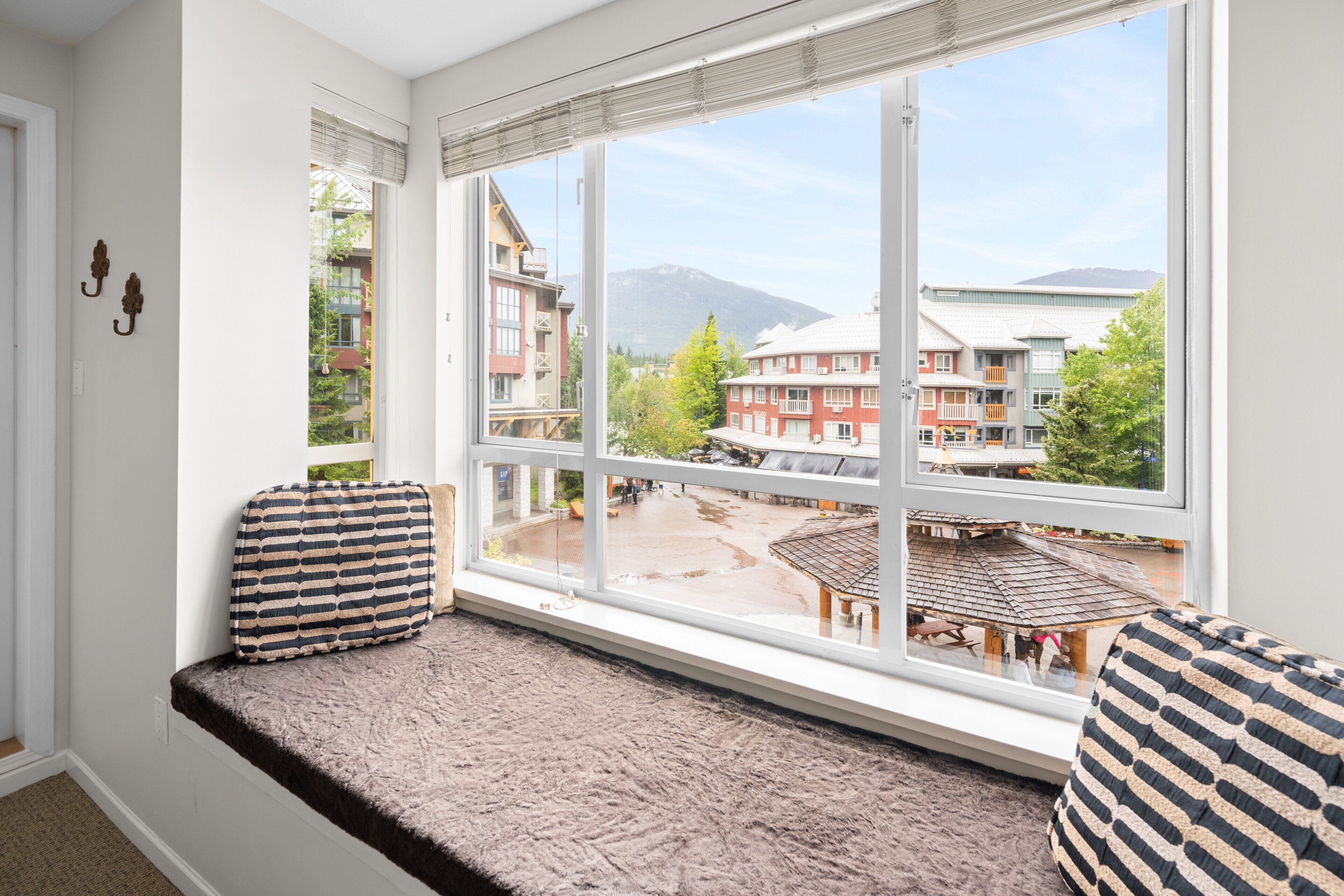 A room with a large window, a bench with striped cushions, and a view of buildings and mountains.