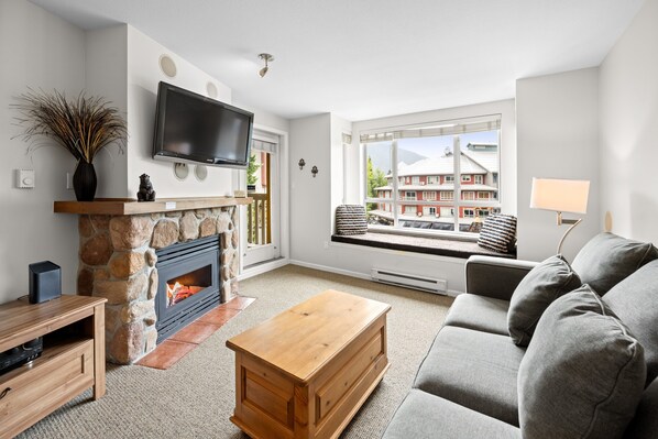 A living room with a stone fireplace, a flat-screen TV, a sofa, and a window with a view of buildings.