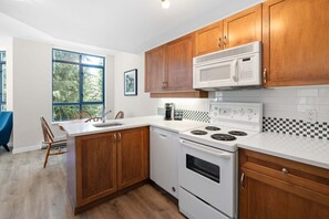 A kitchen with wooden cabinets, a white countertop, a microwave, a stove, and a dishwasher. - Alpenglow Lodge Bear Wonder One-Bedroom by MVA (Whistler)