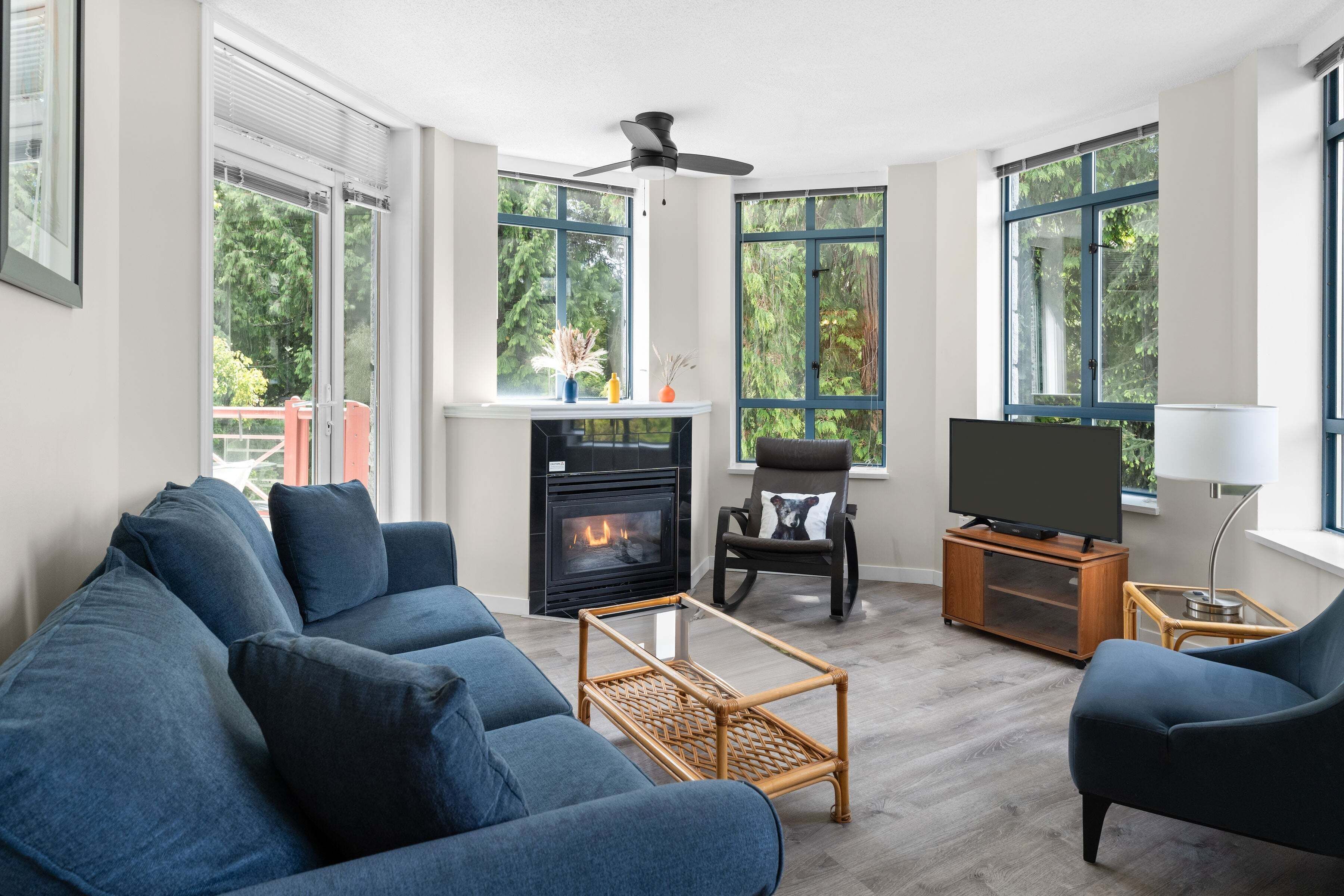 Una sala de estar con sofá, televisor, chimenea y ventanas amplias.