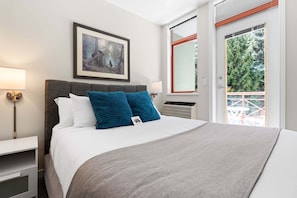 A neatly arranged bedroom with a bed, bedside lamps, a framed picture, and a view through a door. - Alpenglow Lodge Bear Wonder One-Bedroom by MVA (Whistler)