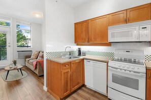 A compact kitchen with wooden cabinets, a white microwave, a stove, and a dishwasher. - Junior One Bedroom Apartment at Whistler Village! (Whistler)