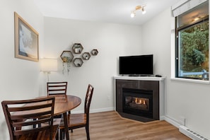 A living room with a fireplace, a television, and a dining area with wooden furniture. - Junior One Bedroom Apartment at Whistler Village! (Whistler)