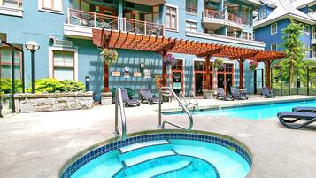 Una piscina con sillas de descanso y un edificio con balcones.