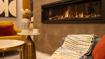 Una sala de estar moderna con chimenea, un sofá amarillo, una mesa de centro redonda y un jarrón decorativo.