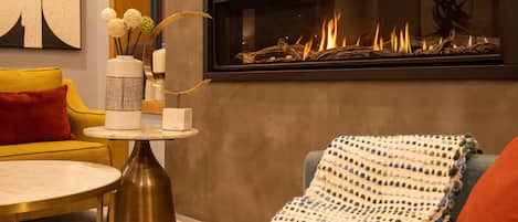 Uma sala de estar moderna com lareira, um sofá amarelo, uma mesa de centro redonda e um vaso decorativo.