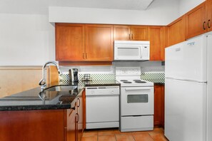 A kitchen with wooden cabinets, a white stove, a microwave, and a refrigerator.