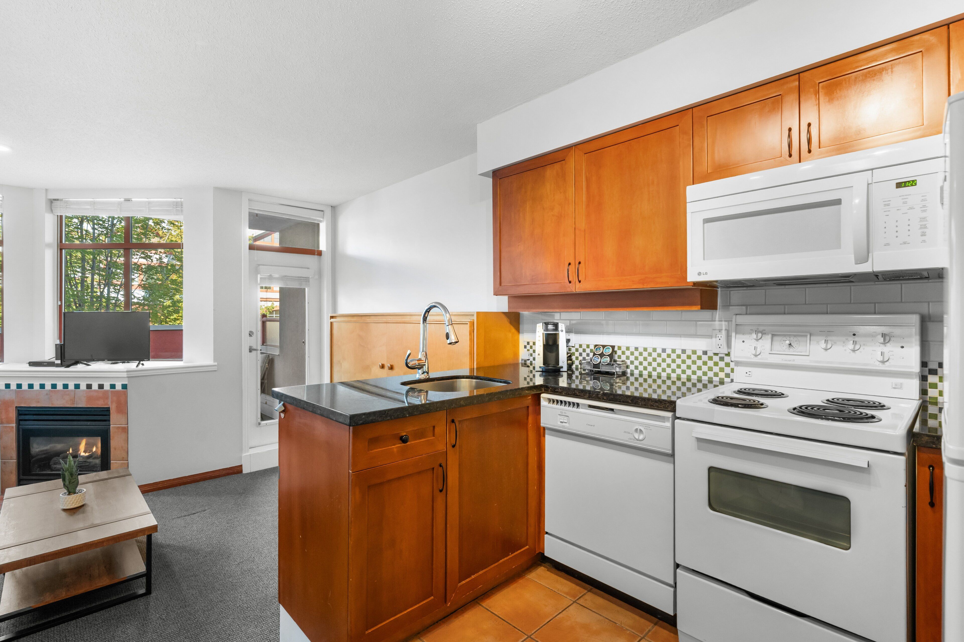 A kitchen with wooden cabinets, a microwave, a stove, a sink, and a television on a fireplace mantel.