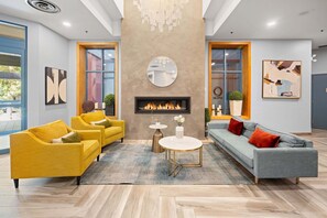 A modern living room with a fireplace, yellow and gray sofas, and a round mirror on the wall.