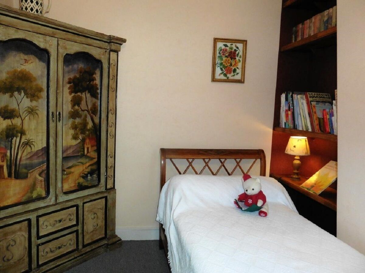Une chambre à coucher comprenant un lit, une tête de lit en bois, une table de chevet avec une lampe, une bibliothèque et une armoire contenant des tableaux.