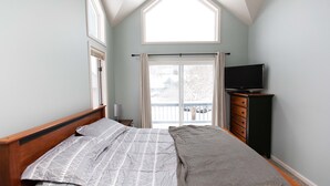 Une chambre à coucher comprenant un lit, une commode, un téléviseur et une fenêtre avec des rideaux.