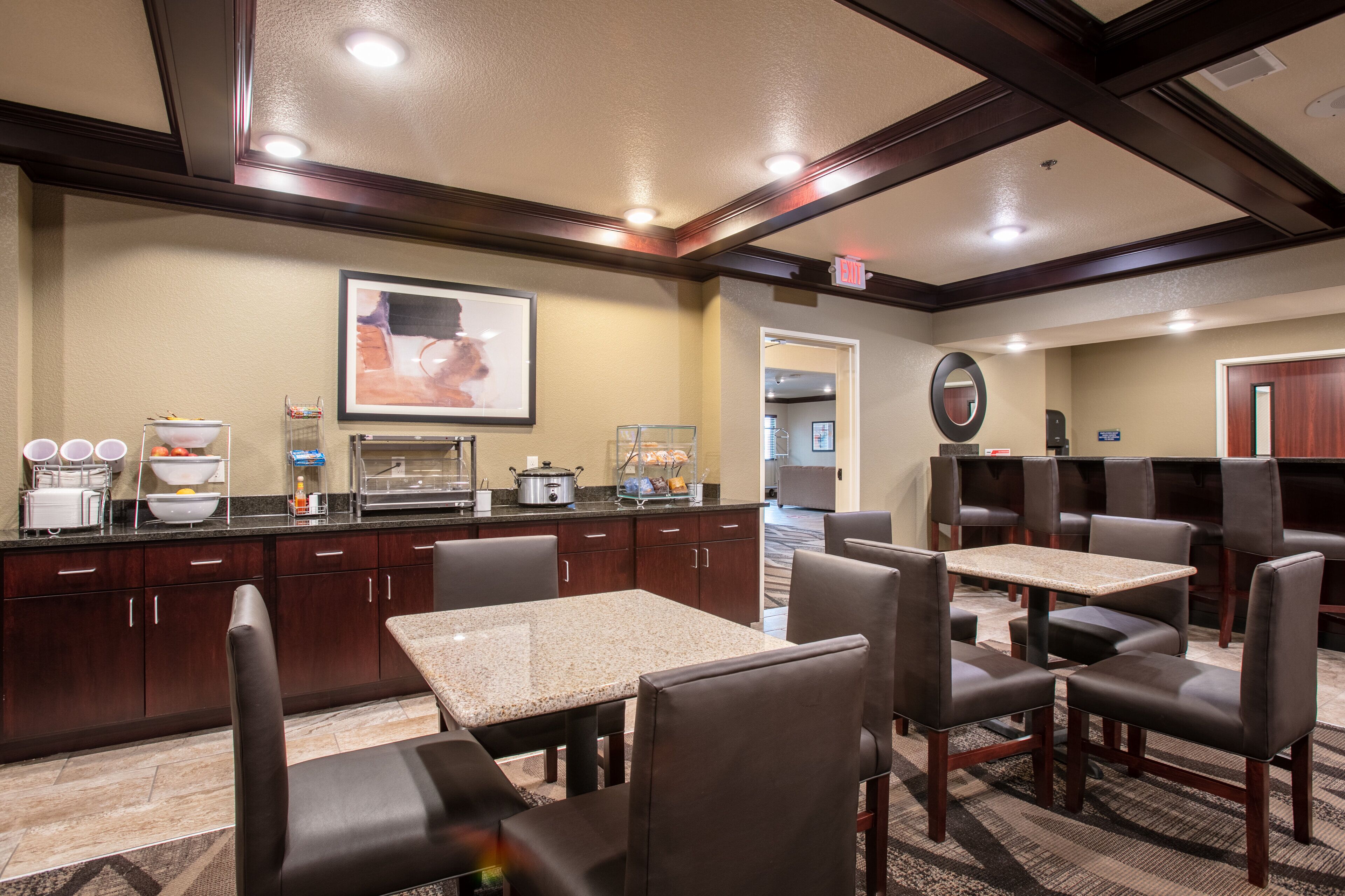 A hotel dining area with a kitchen counter, buffet, and seating.