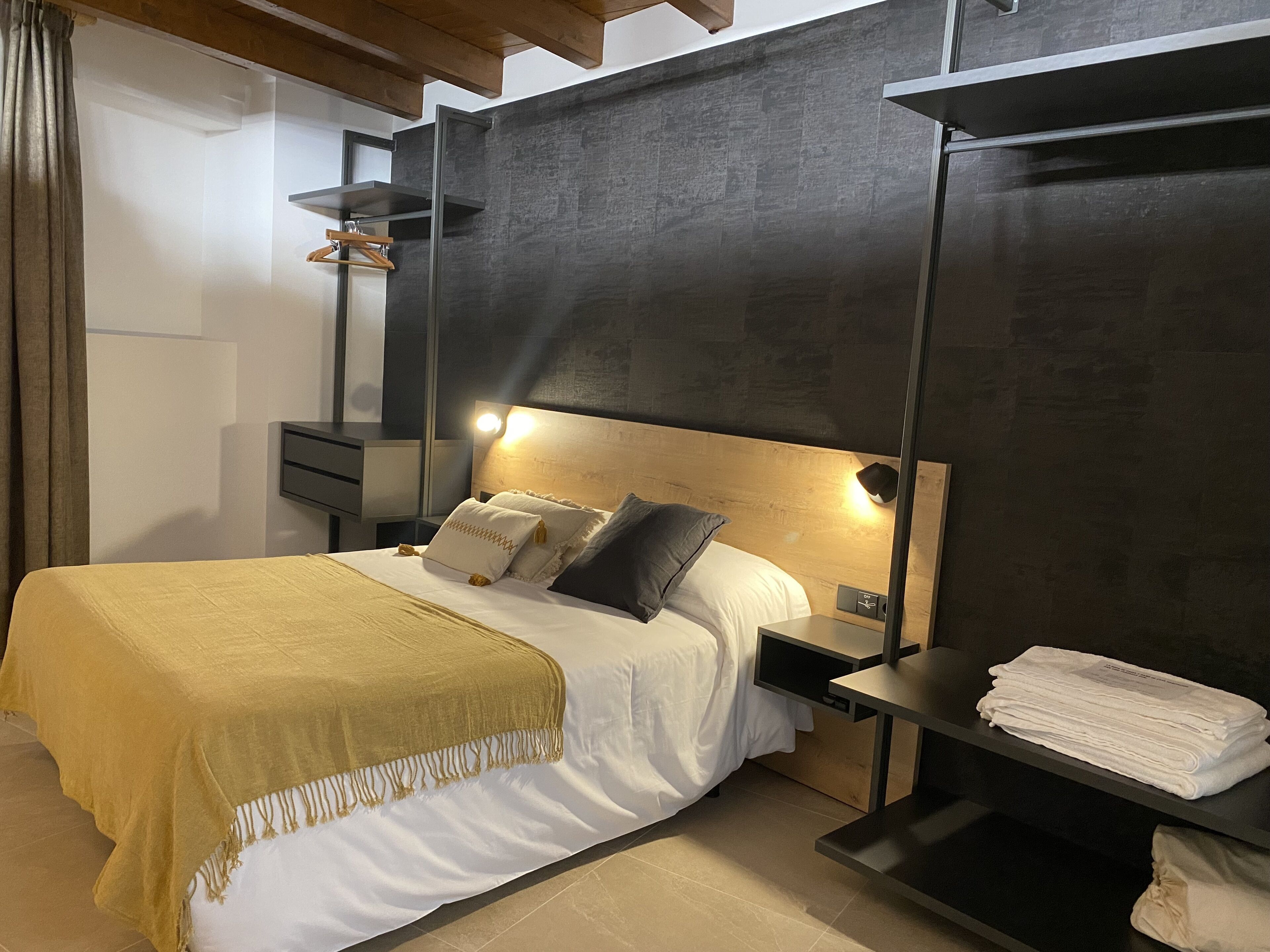 Una camera da letto moderna con un letto, comodini, una lampada a sospensione e uno scaffale con asciugamani piegati.