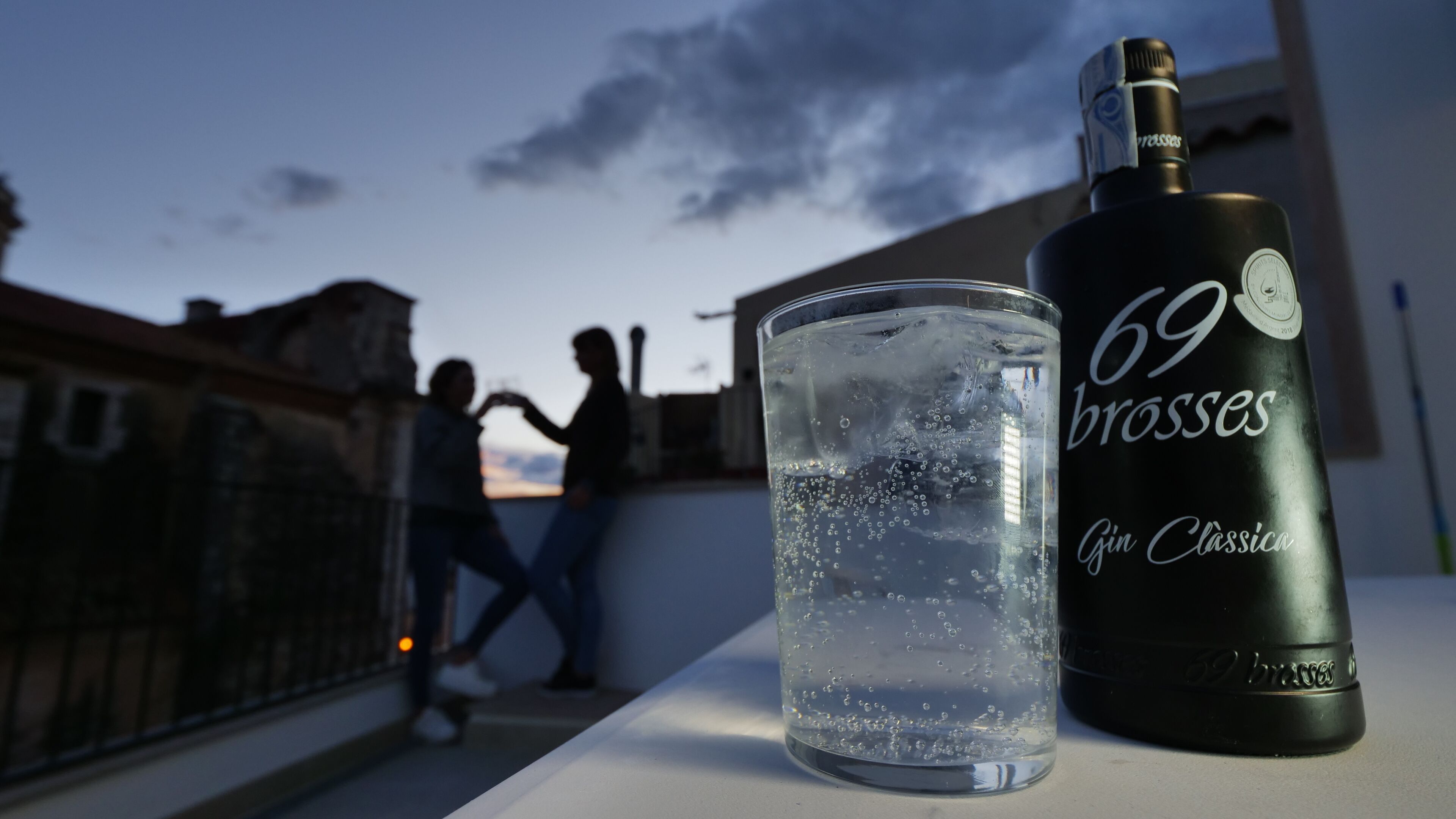 A glass of water and a bottle of 69 Brass gin on a balcony.