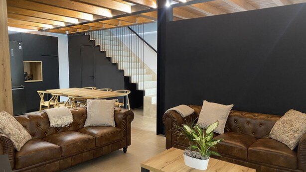 Ein modernes Wohnzimmer mit Ledersofas, einem Holztisch und einer Treppe, die in eine andere Ebene führt.