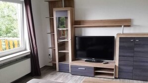 Ein modernes Wohnzimmer mit großem Flachbildfernseher, Holzregalen, einer Couch und einem Couchtisch.