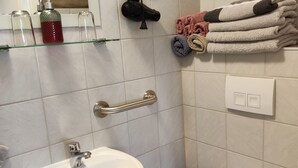 Ein Badezimmer mit weißem Waschbecken, Toilette, Handtuchhalter mit Handtüchern und einem an der Wand befestigten Föhn.
