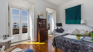 A bedroom with a bed, a dresser, a TV, and a view of the sea through large windows.