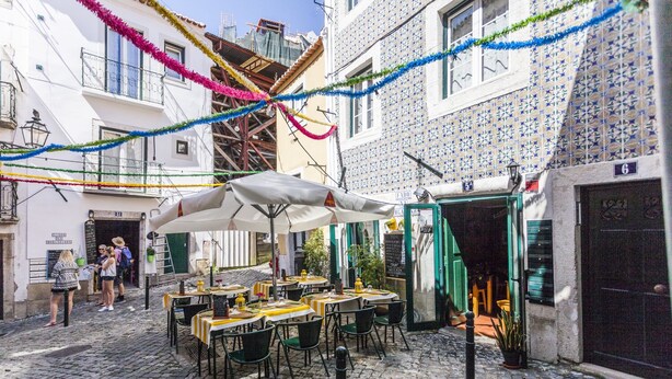 An outdoor café with tables and chairs, a cobblestone street, and buildings with blue and white patterned facades.