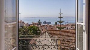 A view from a balcony overlooking a coastal city with terracotta rooftops and a ship in the distance.