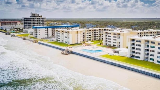 A beachfront hotel with multiple buildings, a swimming pool, and a beach in the background.