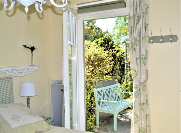 A room with a bed, a lamp, a small table, a bench outside, and a window with curtains. - Charming House by the Sea (Saint-Nazaire)