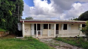 Ein eingeschossiges Gebäude mit Veranda, einem kleinen Anbau und einem Rasen.
