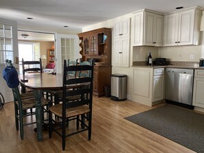 Kitchen area with central island, dining table, and wooden chairs, featuring white cabinetry and a granite countertop.