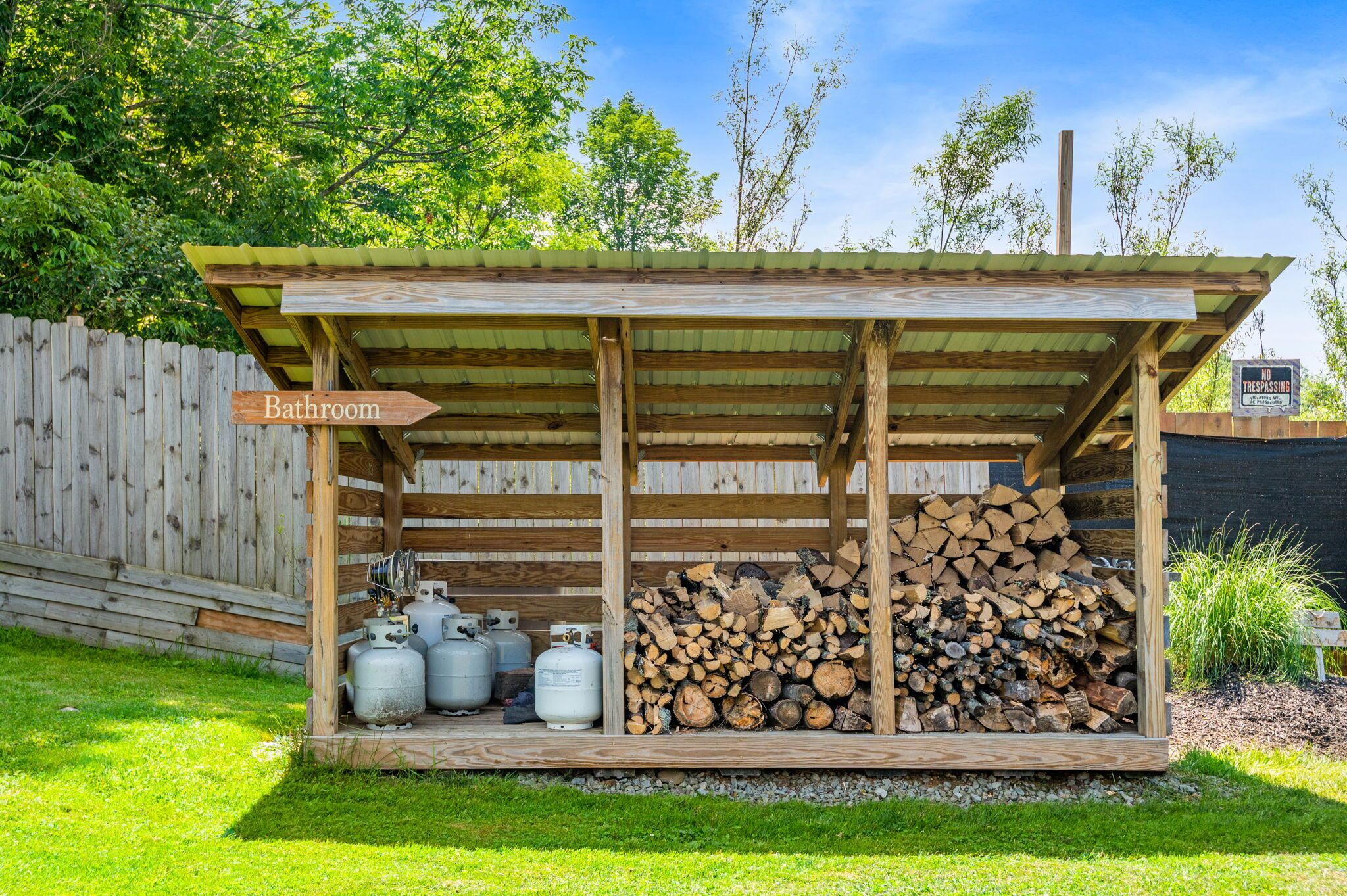 A wooden structure with a roof, labeled 'Bathroom', containing propane tanks and a stack of firewood.