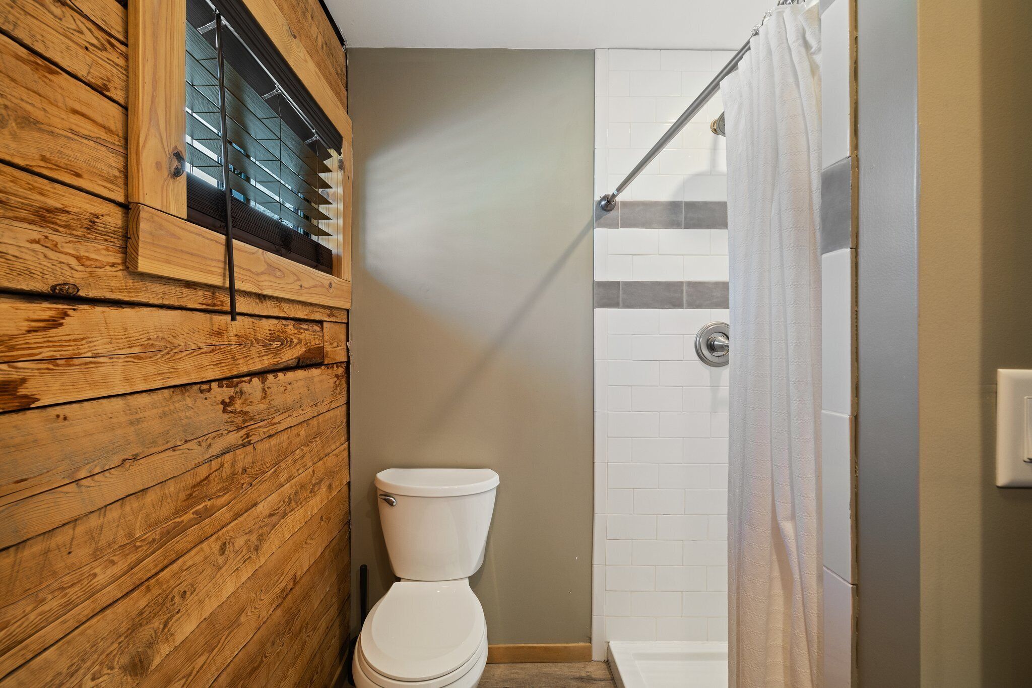 Un bagno con parete in legno, un WC bianco e zona doccia con tenda.