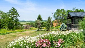 Een tuin met een houten prieel, omringd door verschillende bloemen en bomen.