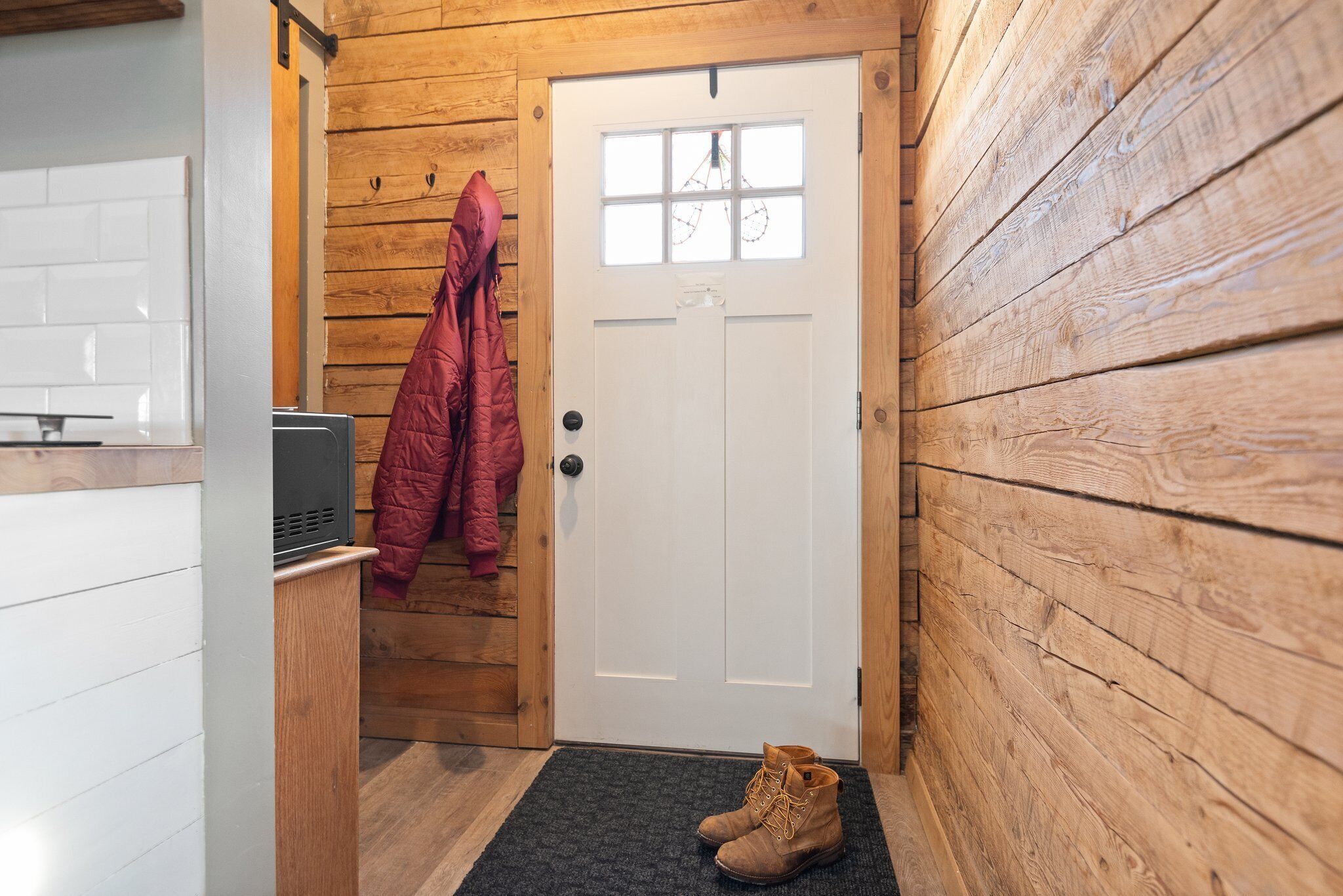 A wooden interior with a white door, a black heater, and a pair of boots on a mat.