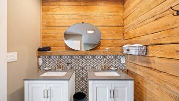 A bathroom with wooden paneling, two sinks, a mirror, and patterned tile backsplash.
