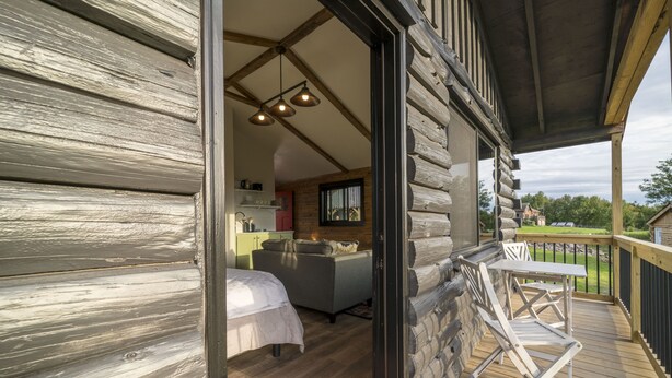 Een blokhut met een houten terras, een gezellige slaapkamer met een bed en een bank, en een eetgedeelte met een tafel en stoelen.