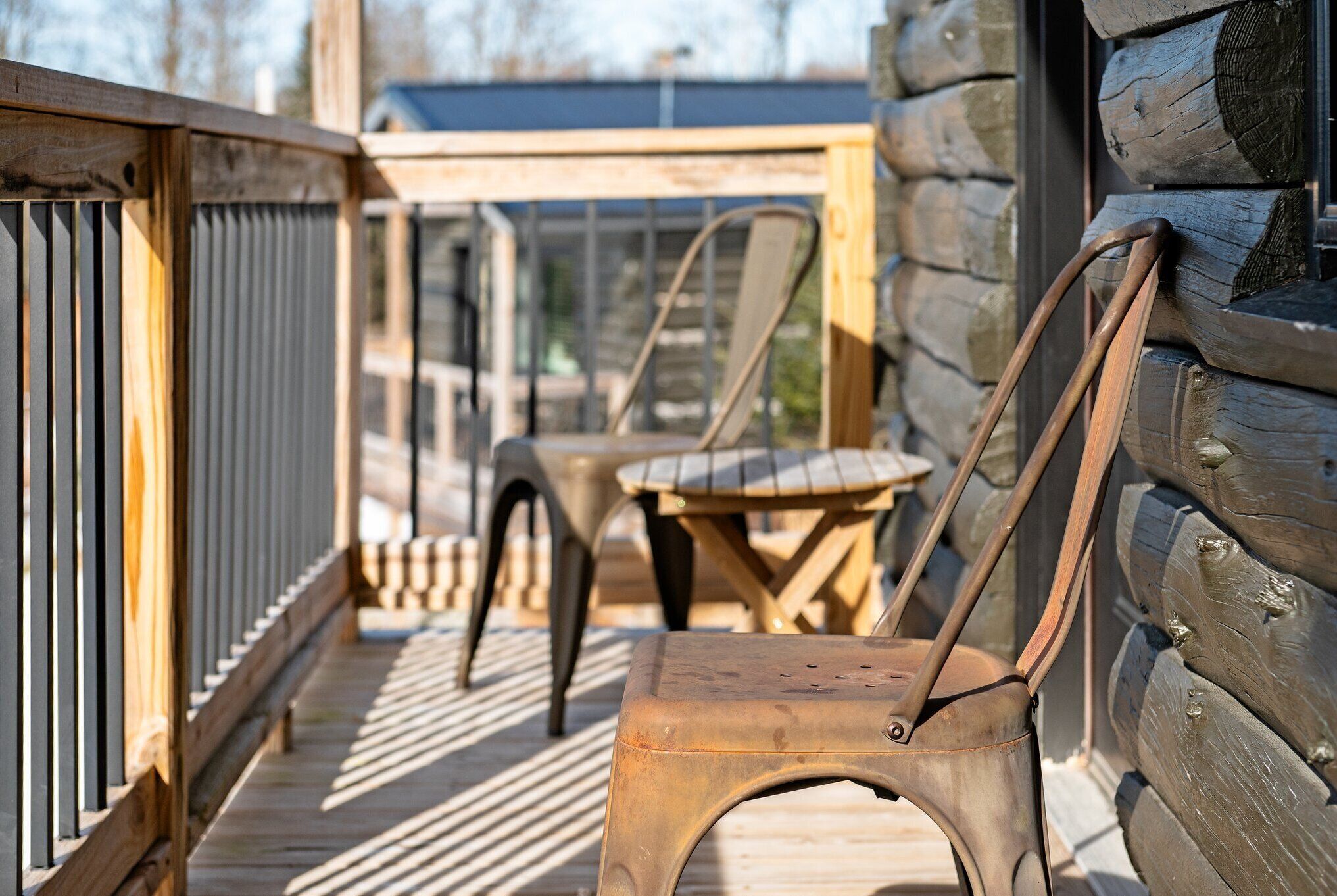 A wooden deck with a metal railing, a wooden chair, and a table.