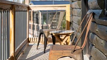 A wooden deck with a metal railing, a wooden chair, and a table.