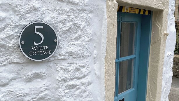 A house number sign for "5 White Cottage" mounted on a textured white wall.