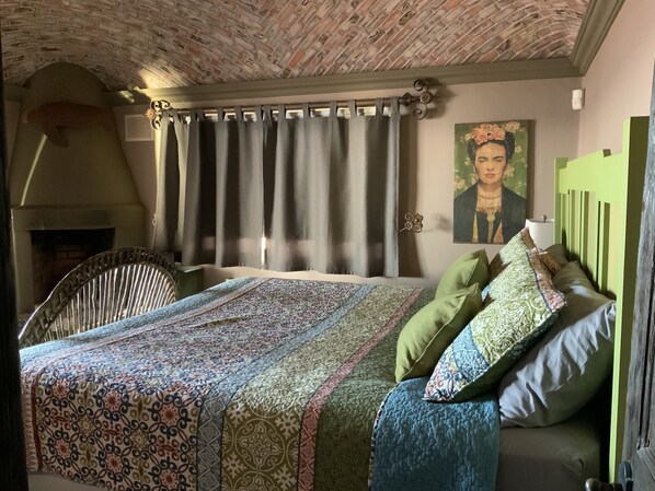 A bedroom with a patterned bedspread, a green headboard, and a painting on the wall.