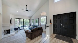 Un salon spacieux avec une cheminée, un ventilateur de plafond et une grande porte noire.